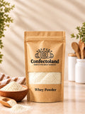 A stand-up kraft paper pouch of Confectoland Whey Powder on a light beige surface, with a small wooden bowl, wooden spoon, and white jars in the background. The pouch has a clear window showing the whey powder inside and black printed branding and text.